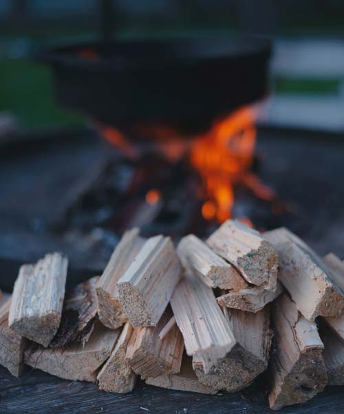 Close up of firewood with an out of focus burning firepit in the background